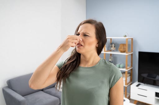 A woman in a home holding her nose because of a bad smell.